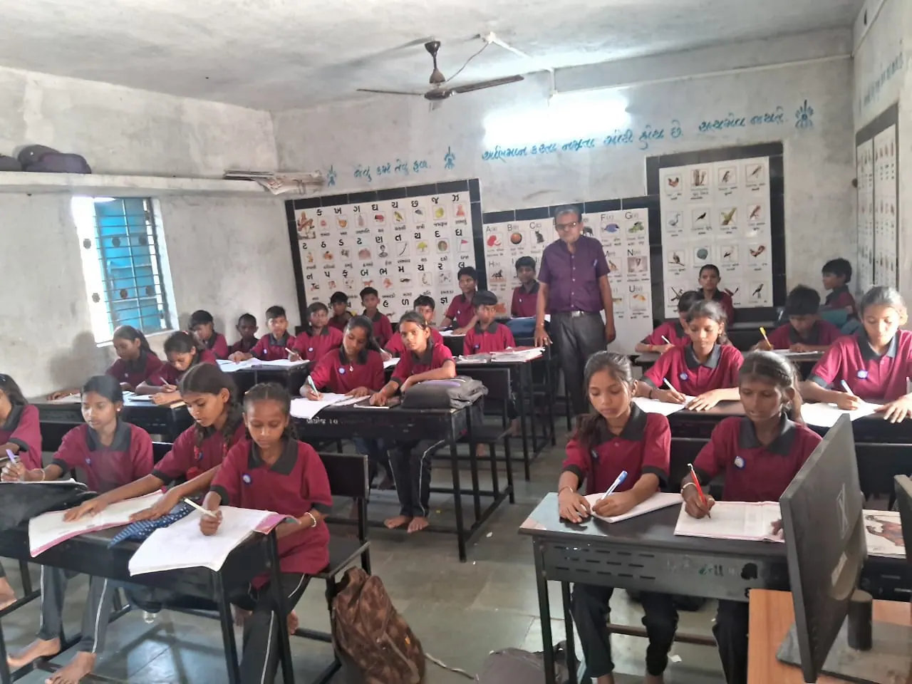 A full classroom of students working in their notebooks at shared desks.